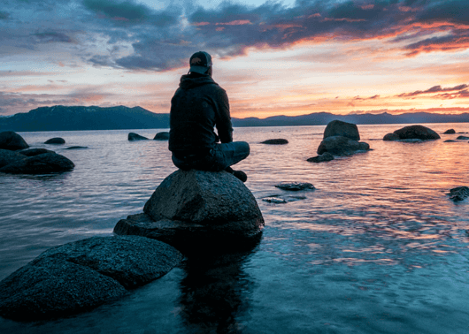 a boy sitting on the rock and watching sunset